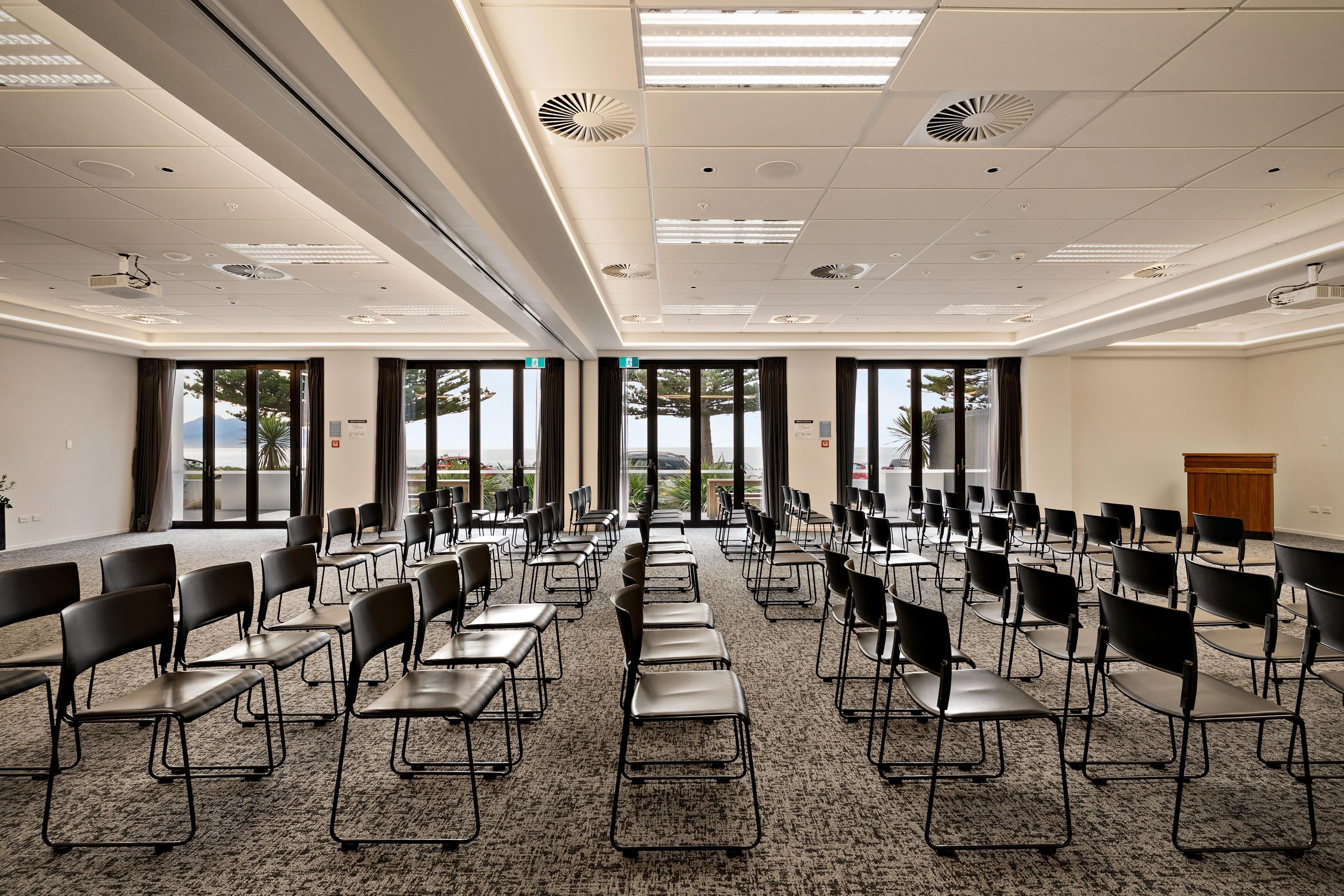 Een vergaderzaal met rijen stoelen, een spreekgestoelte en grote ramen.