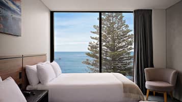 A hotel room with a large window, a bed, a chair, and a painting on the wall.