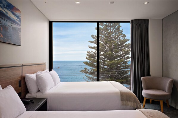 Habitación de hotel con un ventanal grande, una cama, una silla y un cuadro en la pared.