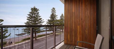 A balcony with a view of a road and trees, wooden paneling, and a wicker chair.