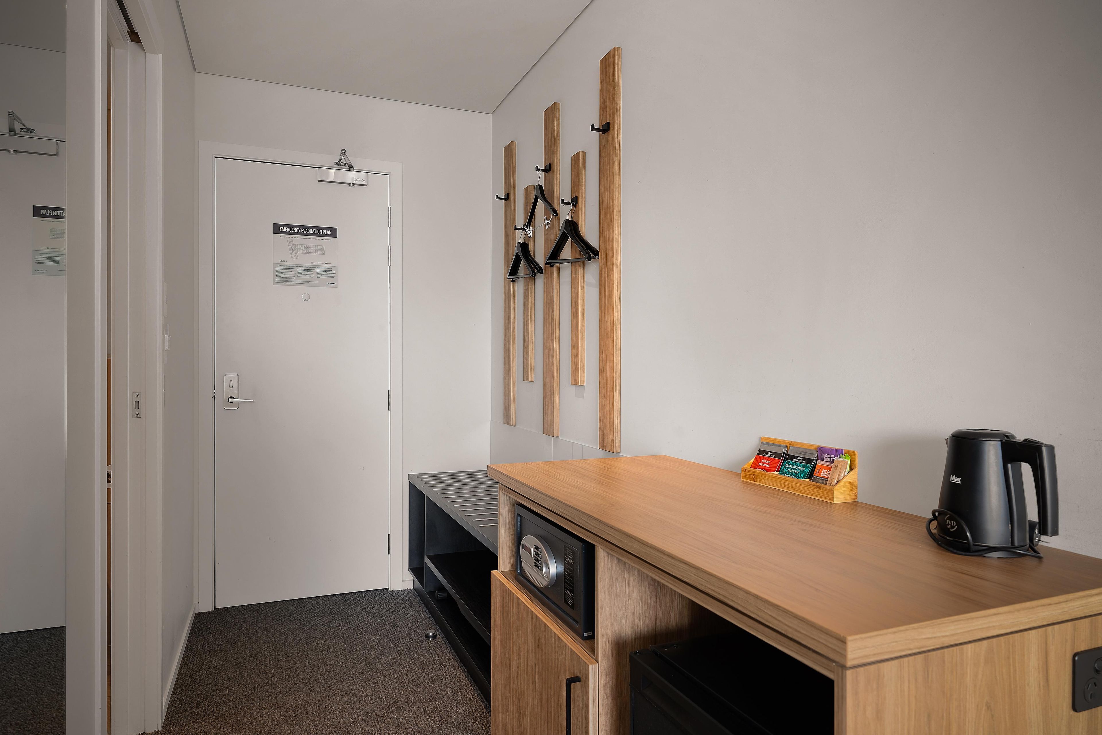 Habitación de hotel con kitchenette, microondas, cafetera y estante de madera con soporte para cápsulas de café.