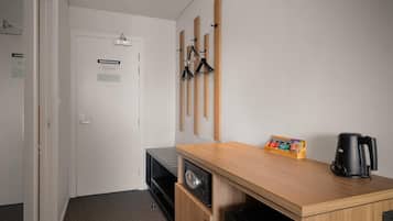 Habitación de hotel con kitchenette, microondas, cafetera y estante de madera con soporte para cápsulas de café.