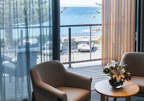 Una habitación con vista al océano, una terraza de madera y una mesa con un jarrón de flores.