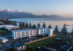 Un hotel moderno con estacionamiento, ubicado cerca de un lago y monta ñas al fondo.