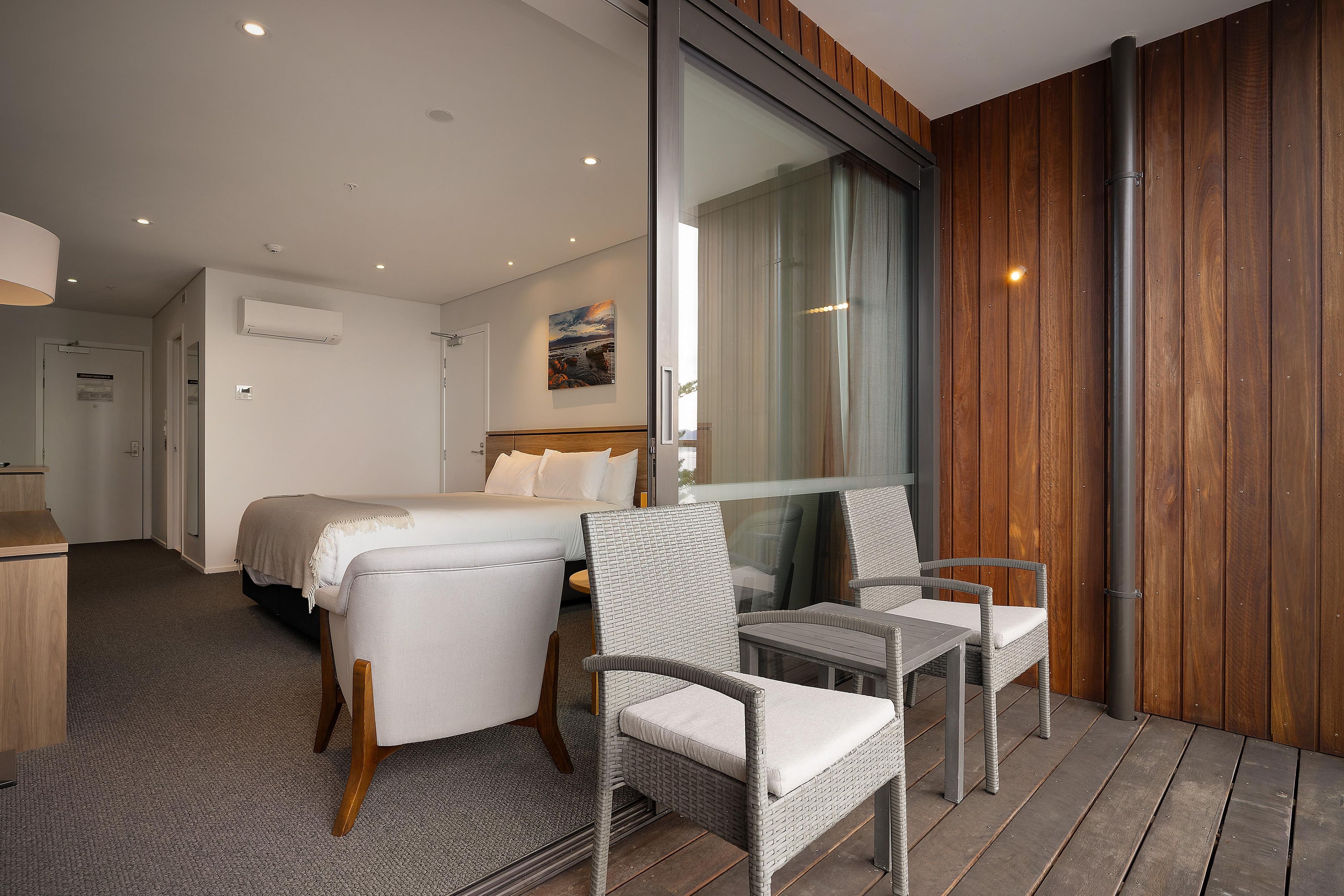 Ein Hotelzimmer mit einem Bett, zwei Stühlen, einem Schreibtisch und einem großen Fenster.