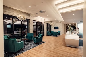 Un vestíbulo moderno con sillones turquesa, un mostrador de recepción y ventanas grandes.