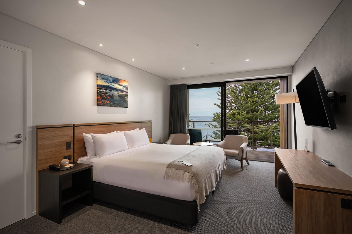Una habitación de hotel moderna con una cama grande, un escritorio, una silla y un televisor.