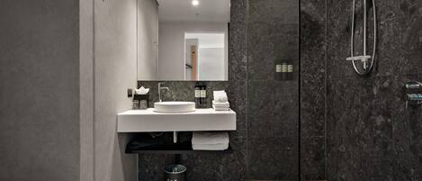 A modern bathroom with a large mirror, a round sink, a glass shower enclosure, and a trash bin.