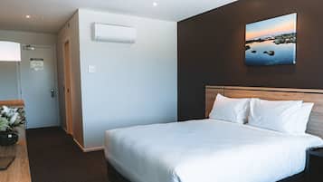 Una habitación de hotel con una cama grande, una mesita de noche, aire acondicionado instalado en la pared y un cuadro de un paisaje.