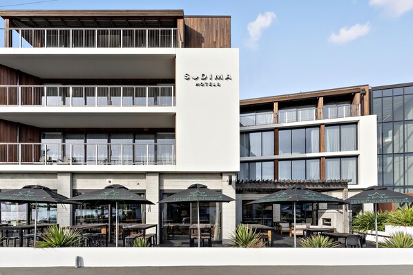 A modern hotel with a two-story structure, outdoor seating with umbrellas, and a clear sky. - Sudima Kaikoura (Kaikoura)