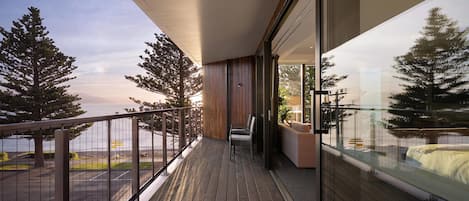 Un balcón con vistas al mar y a los árboles, suelo de madera y una zona de estar con sofá y sillones.