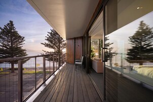 Un balcón con vistas al mar y a los árboles, suelo de madera y una zona de estar con sofá y sillones.