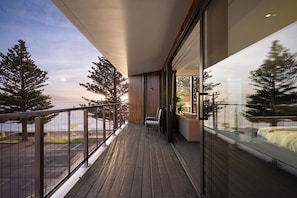 A balcony with a view of the sea and trees, wooden flooring, and a seating area with a sofa and chairs. - Sudima Kaikoura (Kaikoura)