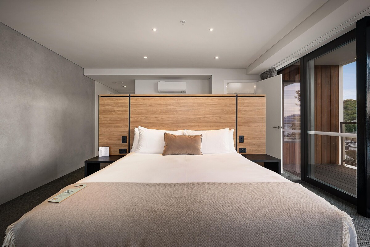 Una habitación de hotel moderna con una cama grande, cabecera de madera y puerta corrediza al exterior.