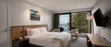 A modern hotel room with a large bed, a desk, a chair, and a TV.