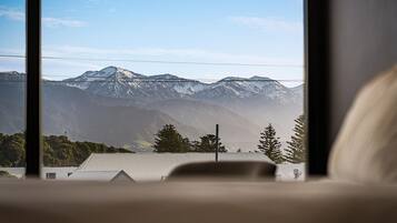 Ein Blick auf schneebedeckte Berge durch ein Fenster, im Vordergrund ein Gebäude und Bäume.