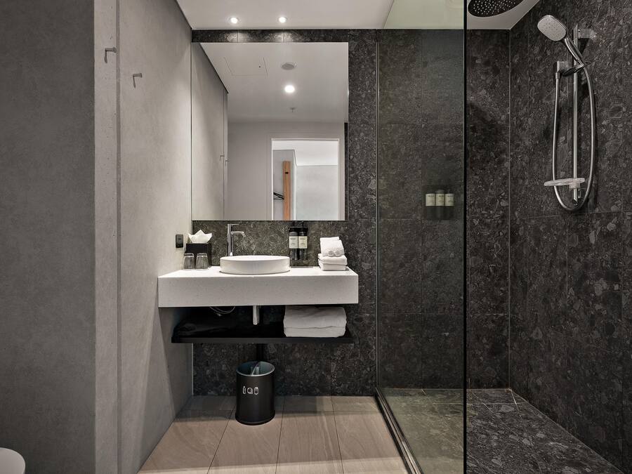 A modern bathroom with a large mirror, a round sink, a glass shower enclosure, and a trash bin.