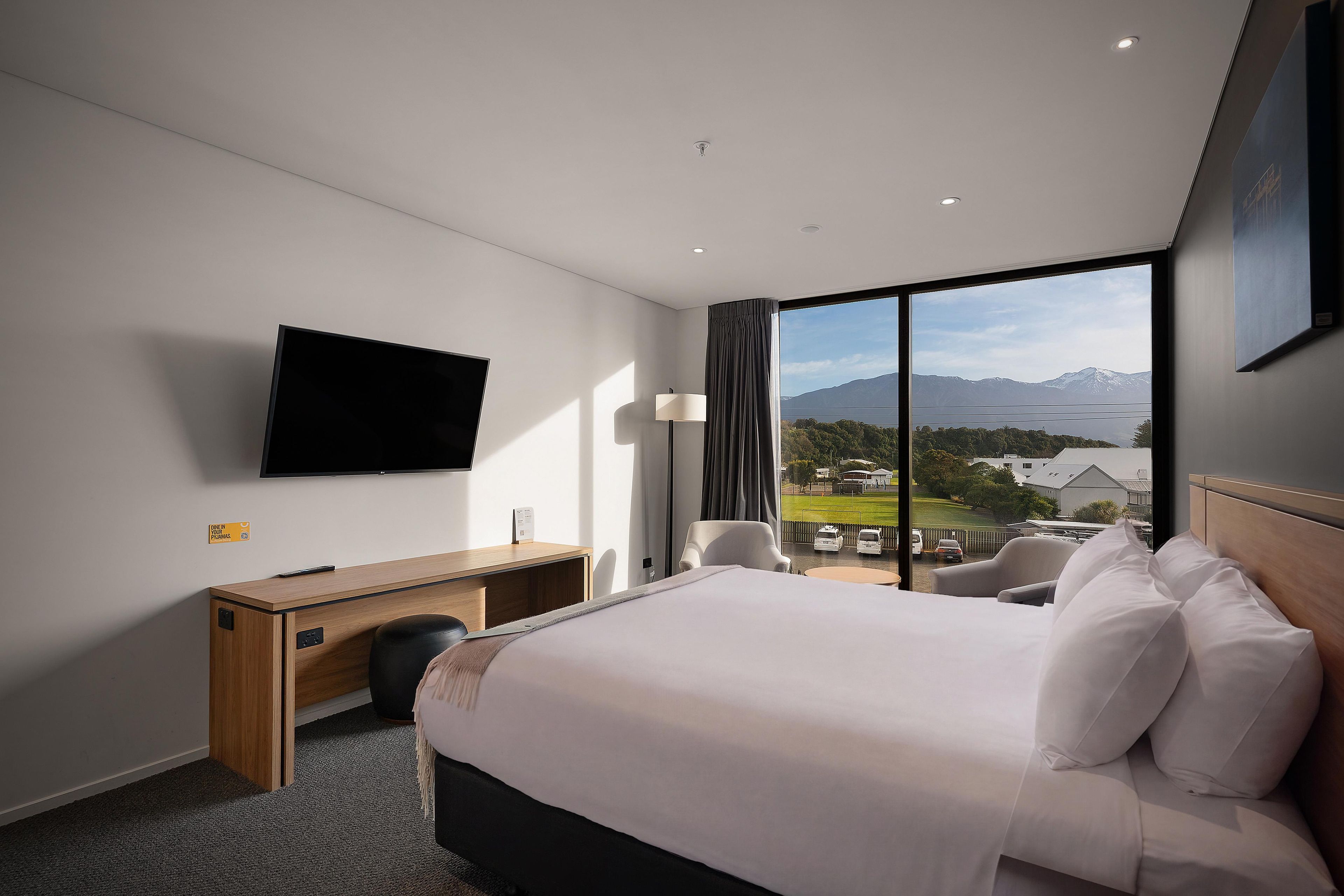 Una habitación de hotel con cama, escritorio, silla, televisor y un ventanal con vistas al exterior.