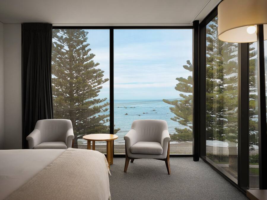 A hotel room with a large window, two armchairs, a small round table, and a bed.