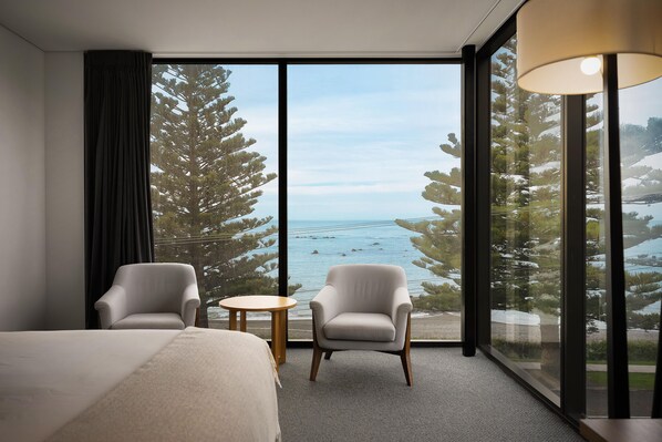 A hotel room with a large window, two armchairs, a small round table, and a bed.