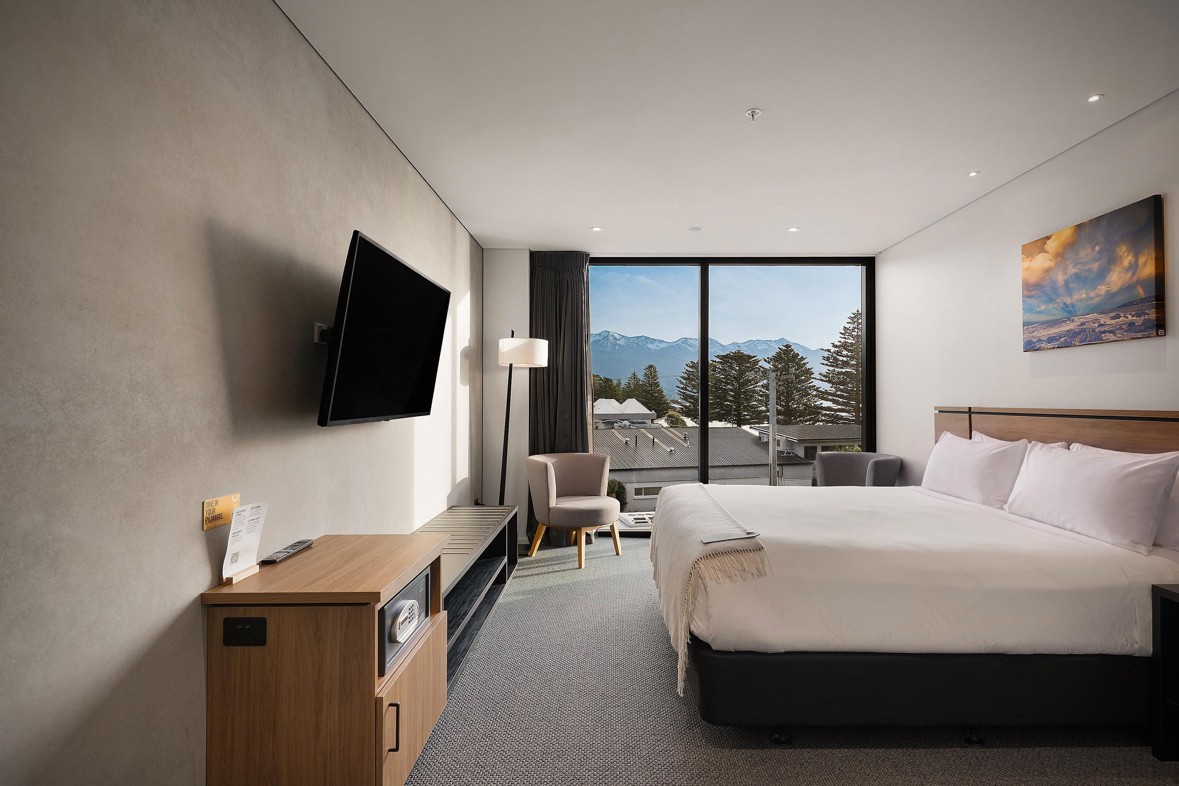 Habitación de hotel con una cama grande, un escritorio, una silla, un televisor y una ventana con vistas a la montaña.