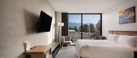 Habitación de hotel con una cama grande, un escritorio, una silla, un televisor y una ventana con vistas a la montaña.
