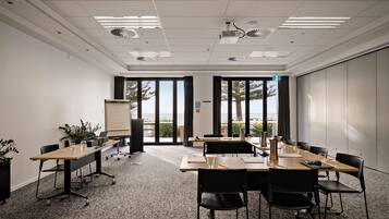 Un salón de conferencias con una pizarra, proyector y grandes ventanales con vistas al exterior.
