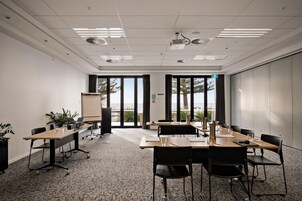 A conference room with a whiteboard, projector, and large windows with a view of the outdoors.