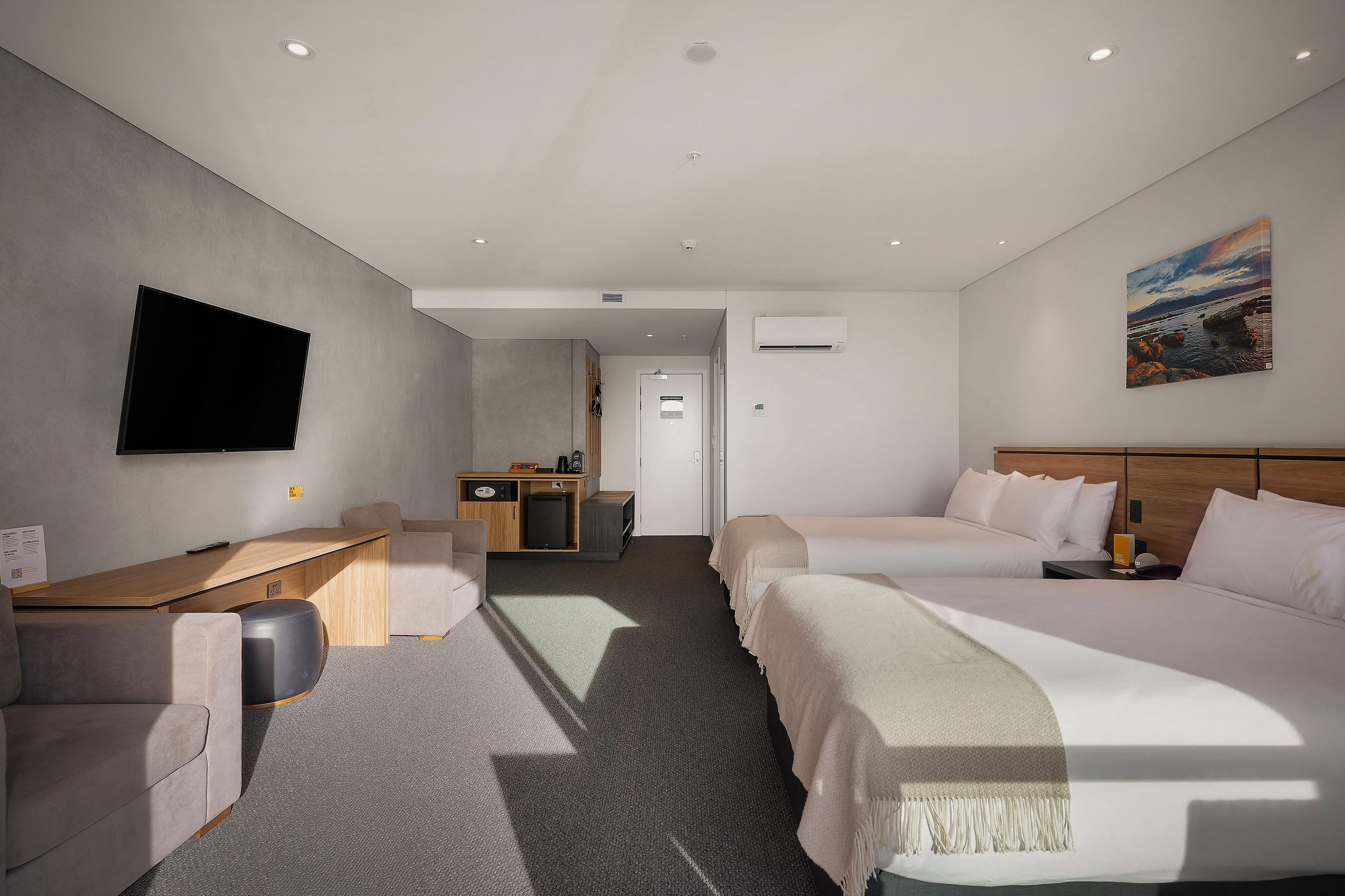 A hotel room with two beds, a desk, a TV, and a painting on the wall.