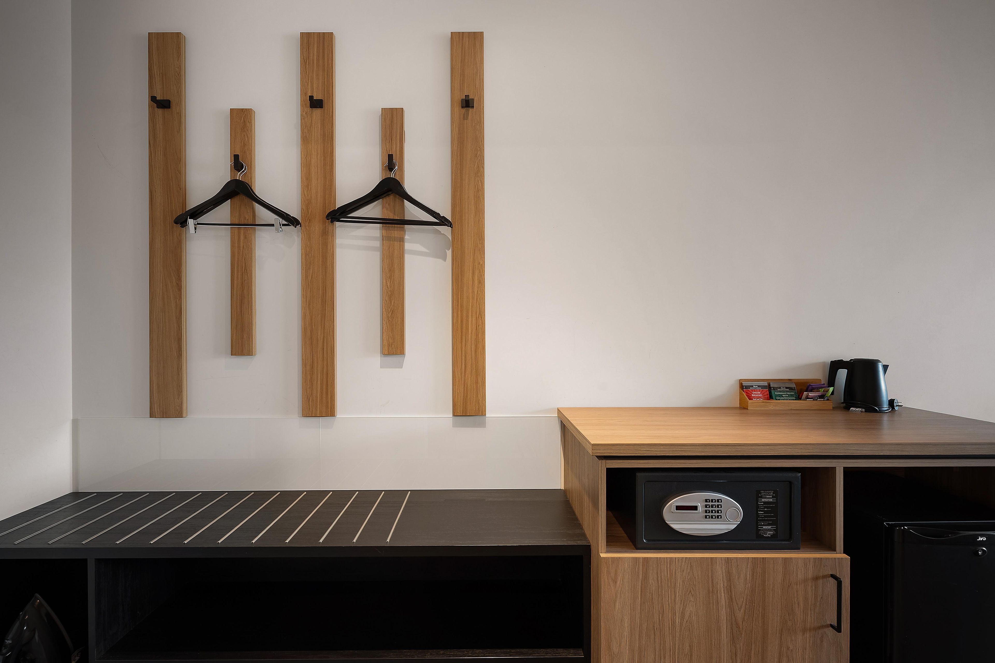 Habitación de hotel con panel de pared de madera, un banco negro, un pequeño armario de madera con microondas y cafetera.