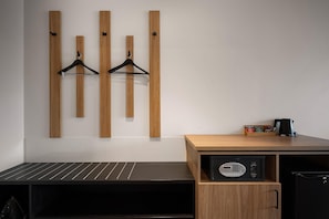 A hotel room with a wooden wall panel, a black bench, a small wooden cabinet with a microwave, and a coffee maker. - Sudima Kaikoura (Kaikoura)