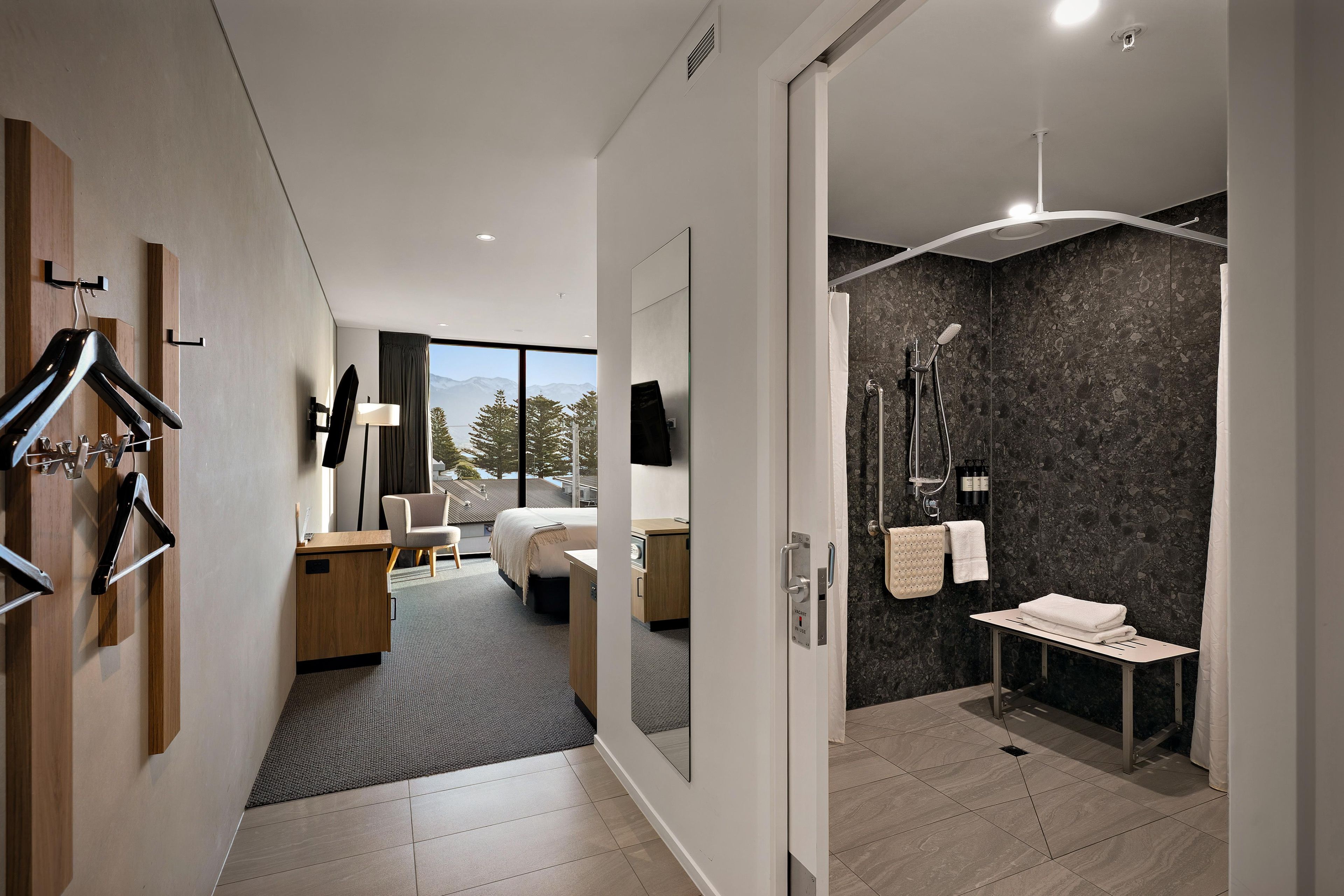A modern hotel room with a bed, desk, and shower area.