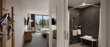 A modern hotel room with a bed, desk, and shower area.