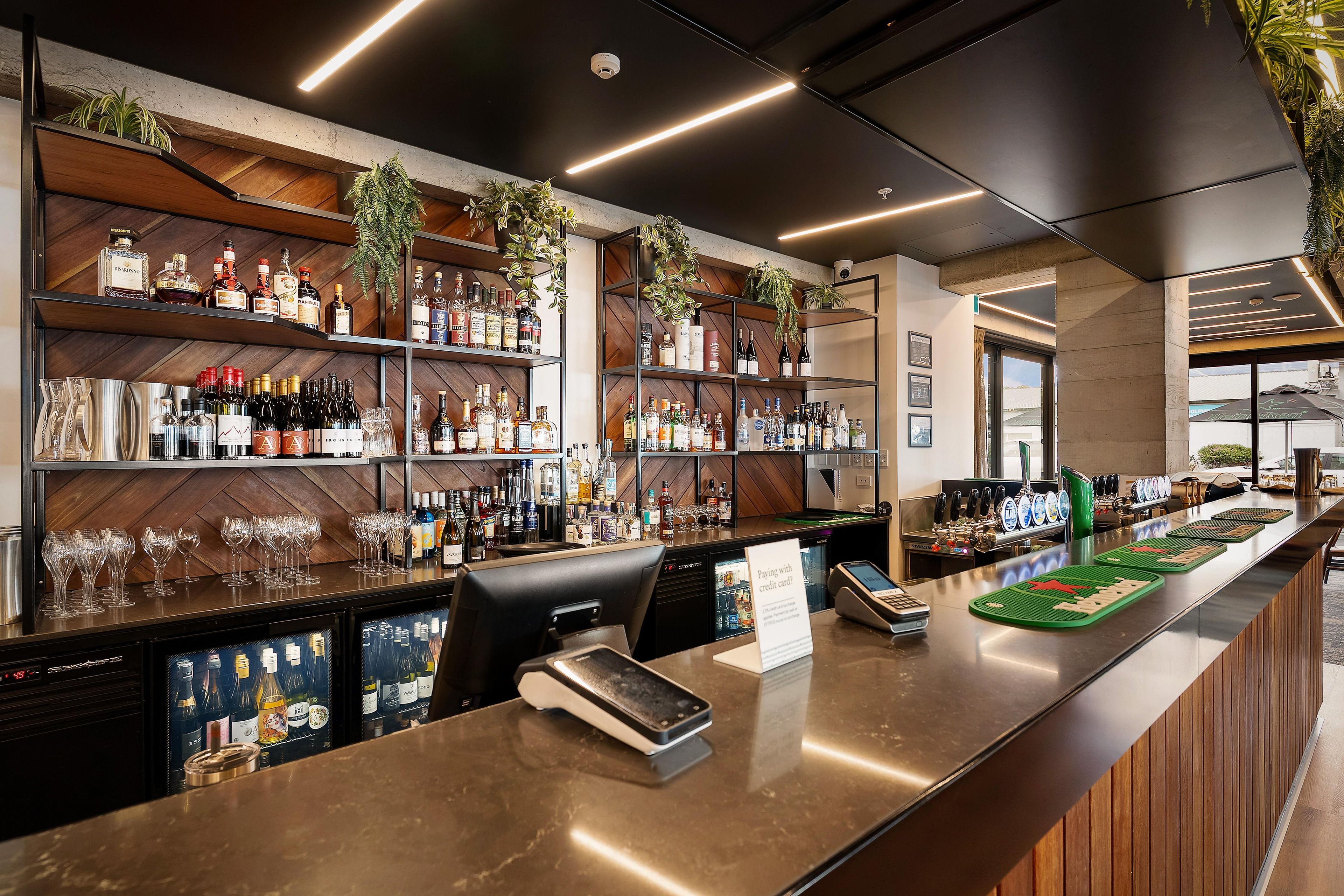 A bar area with shelves of liquor bottles, glasses, and a cash register.