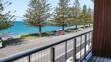 A balcony with a view of a road, trees, and the sea.