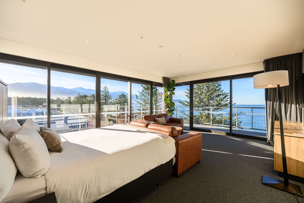Habitación de hotel moderna con una cama grande, un espacio para sentarse y vista al mar.