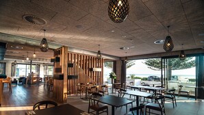 Un restaurant moderne avec des meubles en bois, des luminaires suspendus et de grandes fenêtres offrant une vue sur la mer.