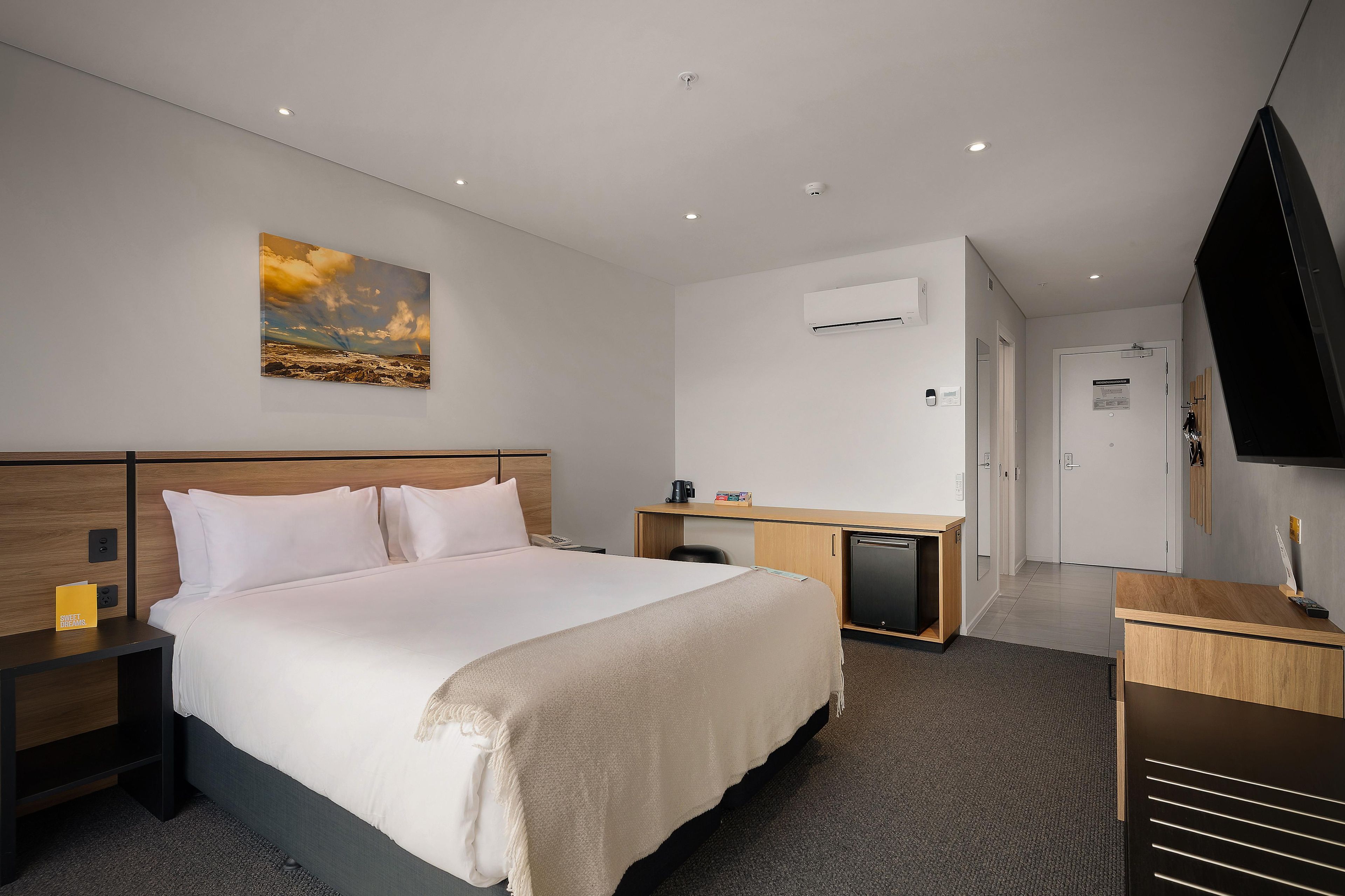 Une chambre d’hôtel équipée d’un lit, de tables de chevet, d’un bureau, d’une chaise, d’une télévision et d’un appareil de climatisation.