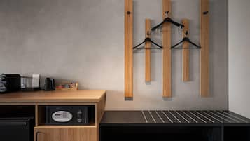 A hotel room with a wooden desk, a coffee machine, a safe, and a wall-mounted coat rack.