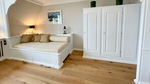 A bedroom with a bed, a nightstand, a lamp, a framed picture, and a wardrobe. - Lovingly designed 62m² apartment offers space for 3 people on the 1st floor. - (Kampen (Sylt))