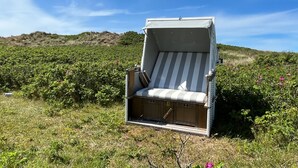 A single-person outdoor lounge chair with a striped cushion, set on a grassy field with a hill in the background. - Lovingly designed 62m² apartment offers space for 3 people on the 1st floor. - (Kampen (Sylt))