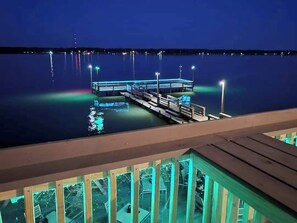 A dock extending into calm water at night with lights reflecting on the surface. - Under the Pines on Lake Livingston- BEAUTIFUL WATER VIEW! (Onalaska)