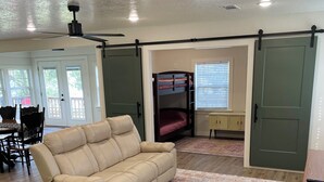 Ein geräumiges Wohnzimmer mit einem beigefarbenen Sofa, einem gemusterten Teppich und einem Schlafstockbett im Hintergrund.