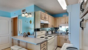 Una cocina con armarios de madera clara, una estufa blanca y una pared azul decorativa.