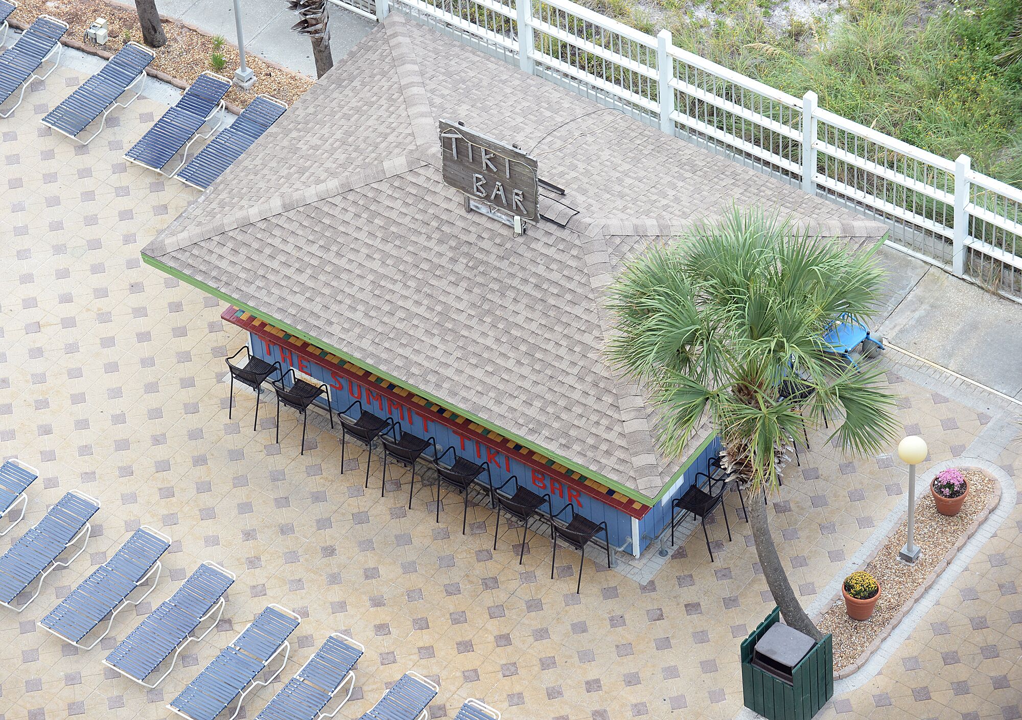 A tiki bar with a tiled roof, outdoor seating, and a palm tree.