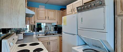 Una cocina con armarios de madera, estufa blanca, fregadero, refrigerador y lavadora.