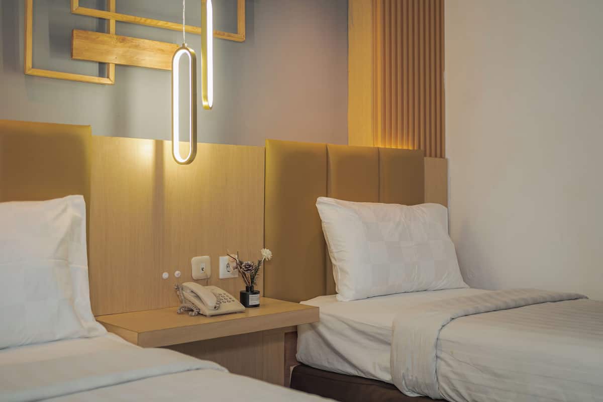 Habitación de hotel con dos camas, una mesita de noche con teléfono y una lámpara fijada a la pared.
