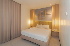 A hotel room with a large bed, a headboard with integrated lighting, a bedside table with a lamp, and a wall-mounted artwork. - Best Hotel (Surabaya)