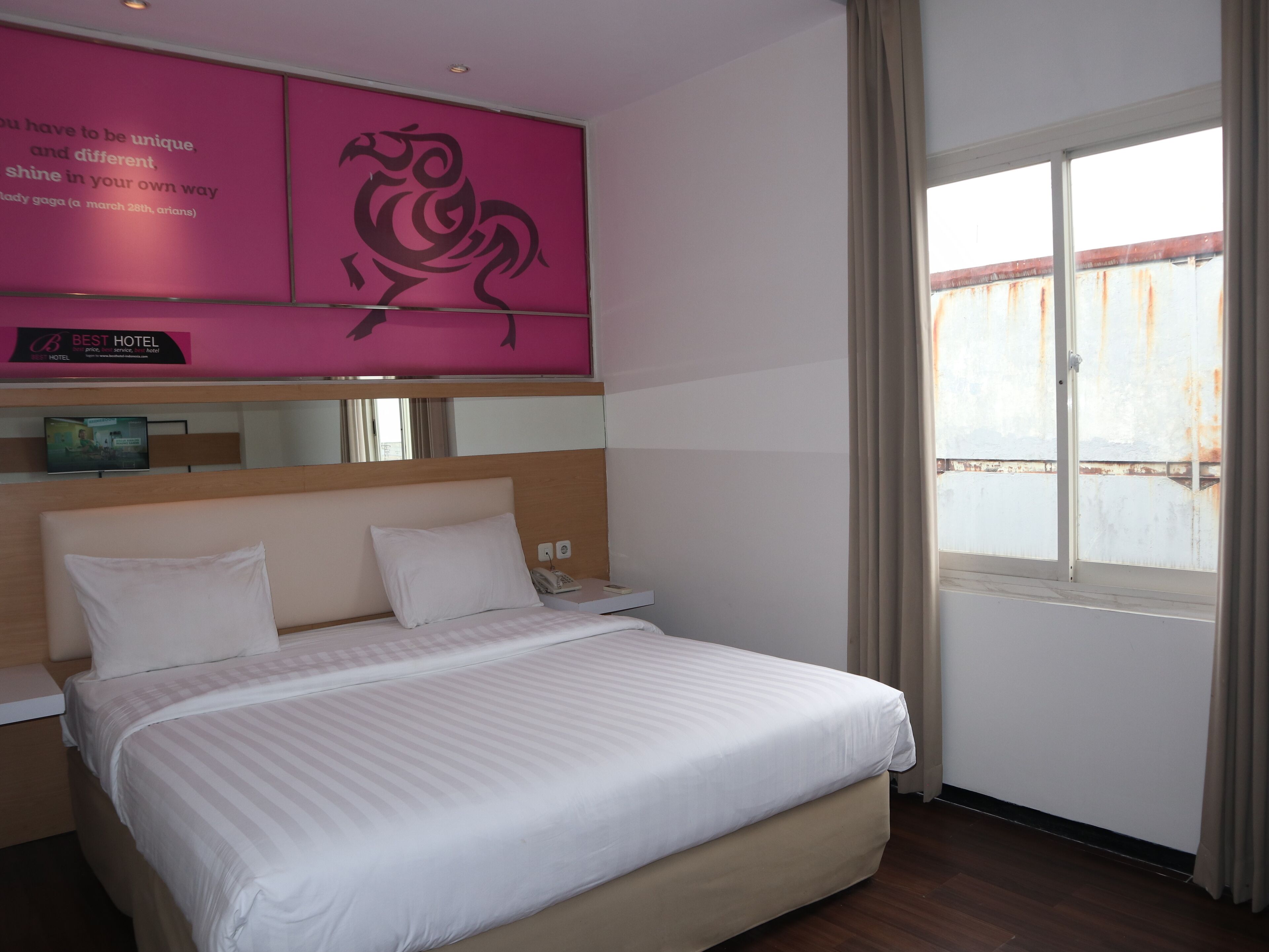 A hotel room with a bed, a television, and a window with curtains.