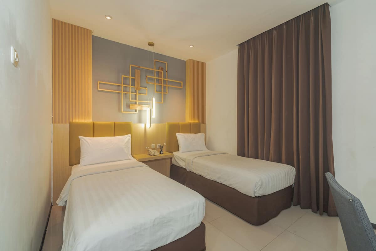 Habitación de hotel con dos camas, una lámpara de pared y un amplio ventanal con cortinas.